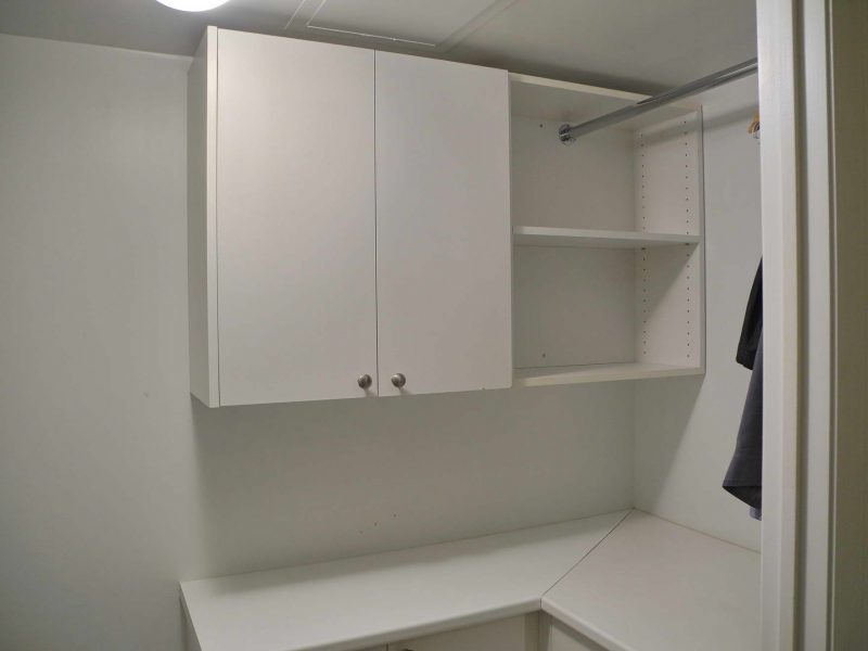 The south side of the laundry room, has both upper and lower cupboards, counter space and a clothes hanging bar